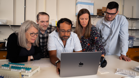 Five people huddled around a laptop in a laboratory.